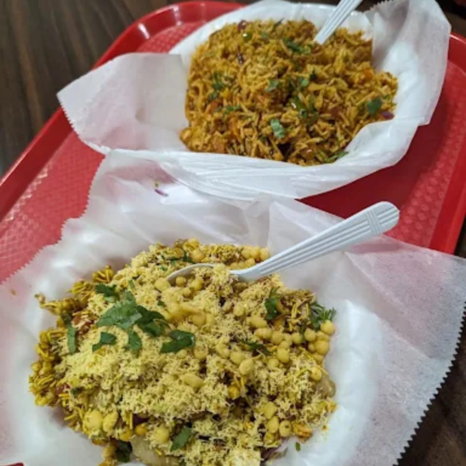 Two Indian dishes, one with rice and the other with chickpeas and crispy toppings, on a red tray.