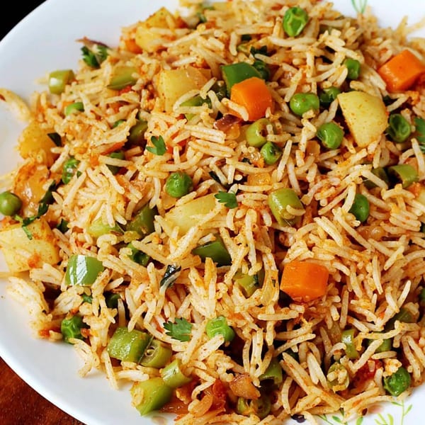 A close-up of Indian vegetable pulao with rice, peas, carrots, and potatoes on a white plate.