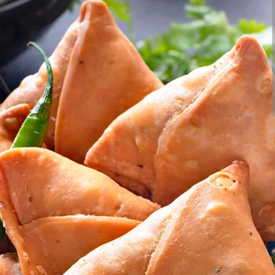 Close-up of golden-brown Indian samosas with a green chili and cilantro in the background.