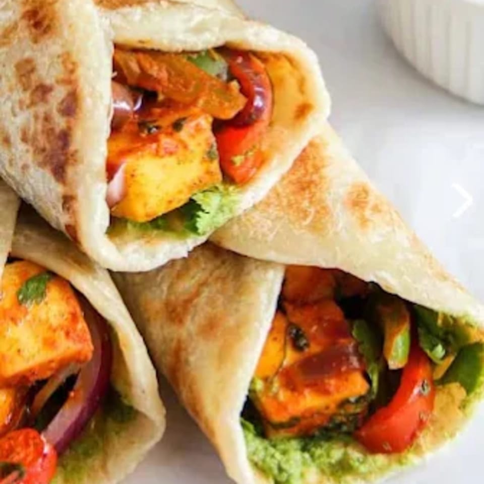 Two Indian paneer kathi rolls, filled with paneer, red onions, and peppers, on a white surface.