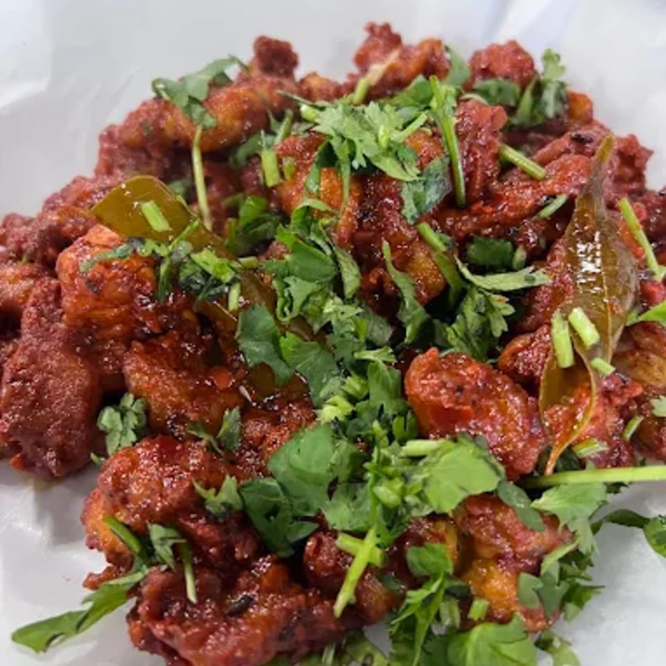 Chai Wyy's Indian chicken dish, vibrant red, garnished with fresh green cilantro and curry leaves.