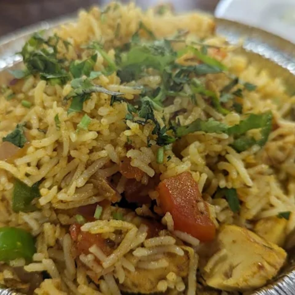 Close-up of Indian biryani with rice, chicken, tomatoes, and cilantro in a foil container.