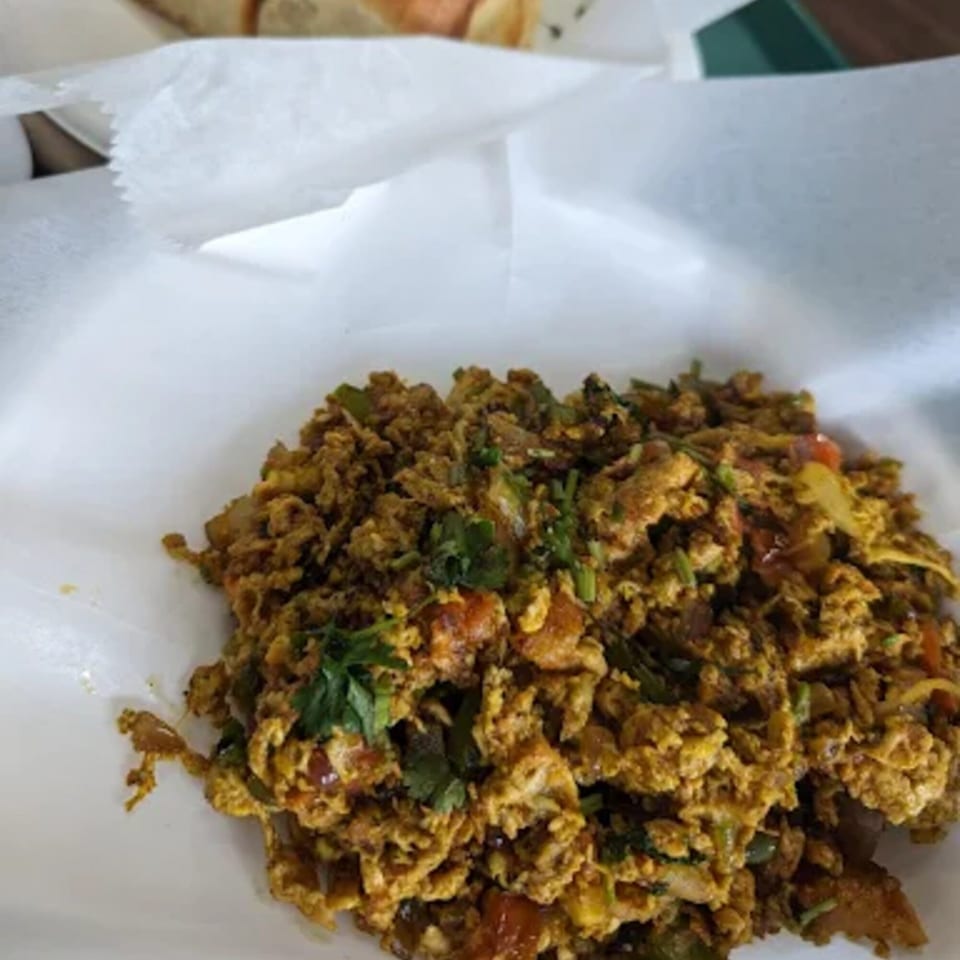 Close-up of Indian scrambled eggs (Anda Bhurji) with herbs and spices, served in white paper.